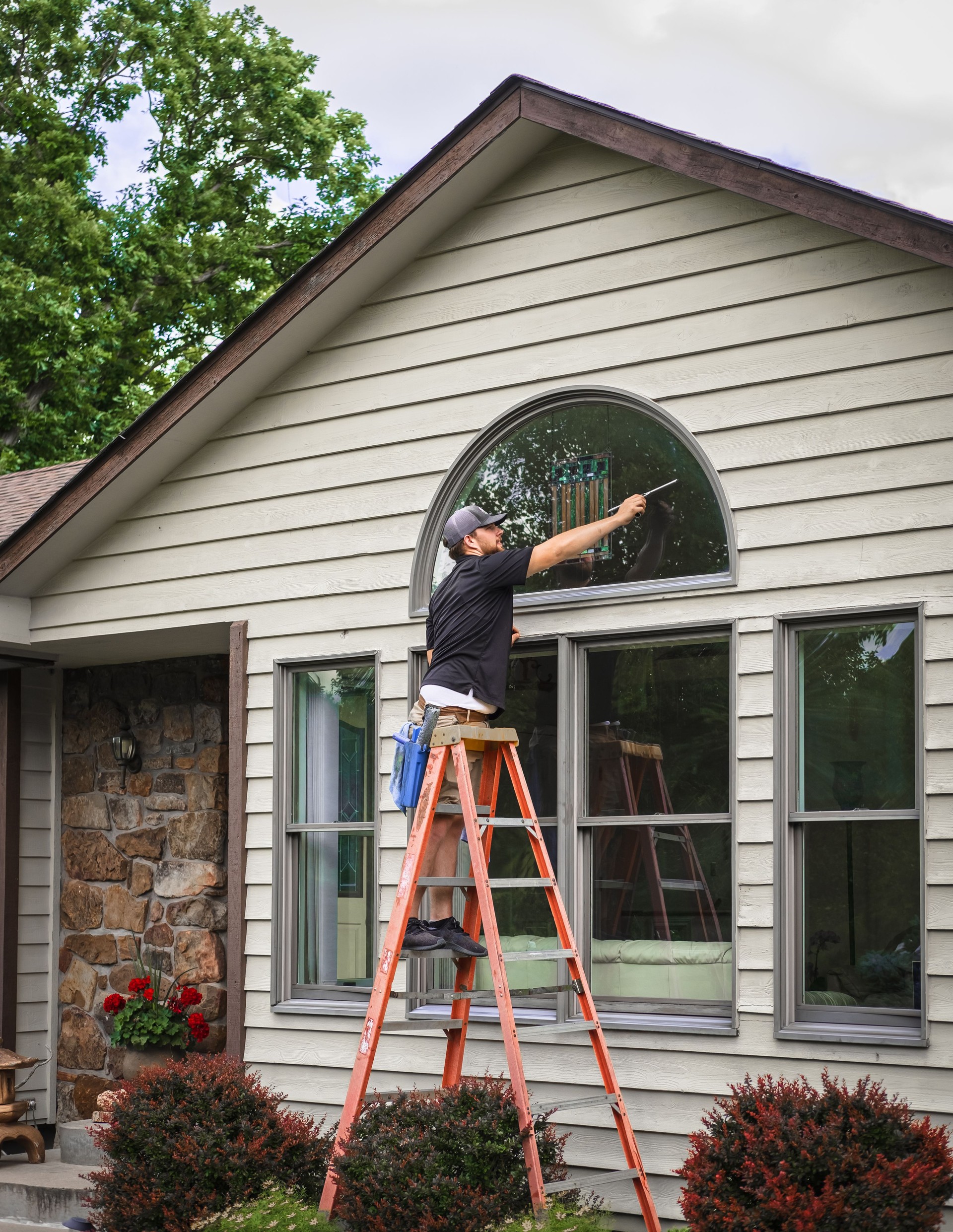Young man standing on ladder washing outside windows of Midwestern house